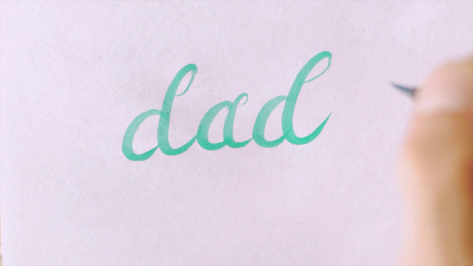 Hand Writing The Word Dad In Cursive On White Paper - Dad In