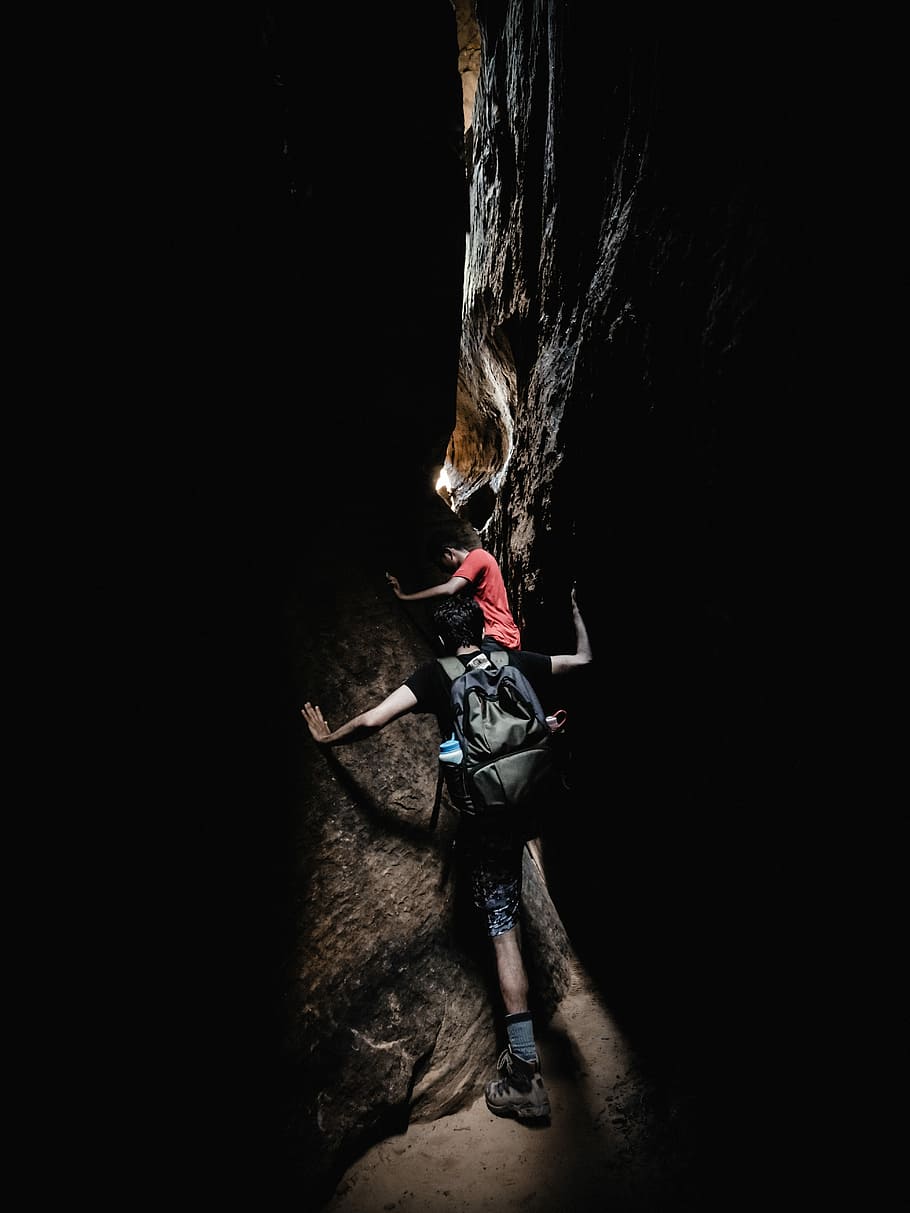 Two Boy S Climbing Between Black And Grey Rocks During - Speleology - HD Wallpaper 